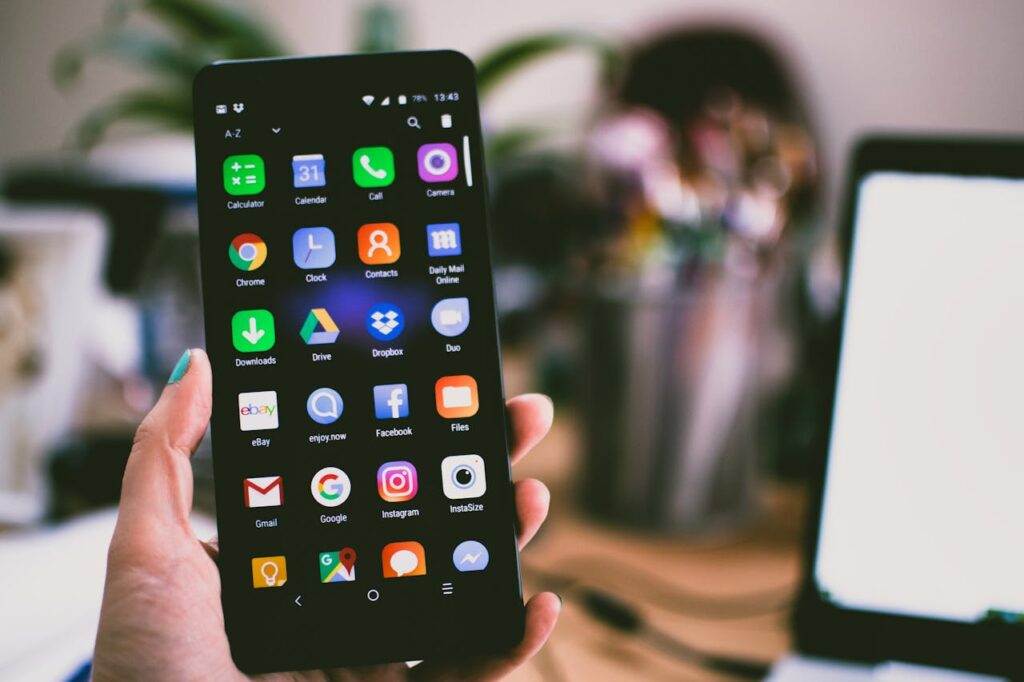 sotsiaalmeedia haldus A close-up image of a person's hand holding a smartphone displaying various popular apps.